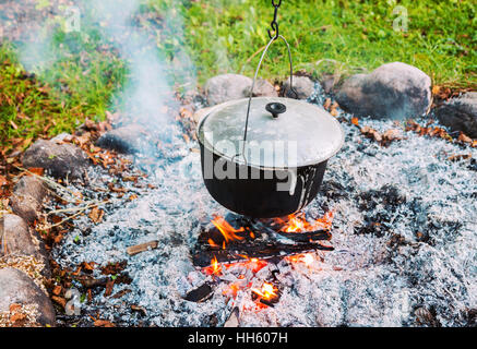 Over the fire hangs a pot in which to cook food. On a hook on a tripod,  steam comes out of the pan. Winter Camping outdoor cooking Stock Photo -  Alamy