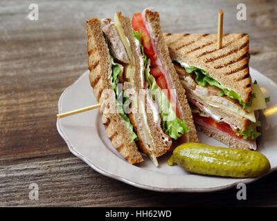 Photo of a club sandwich made with turkey, bacon, ham, tomato, cheese, lettuce, and garnished with a pickle. Stock Photo