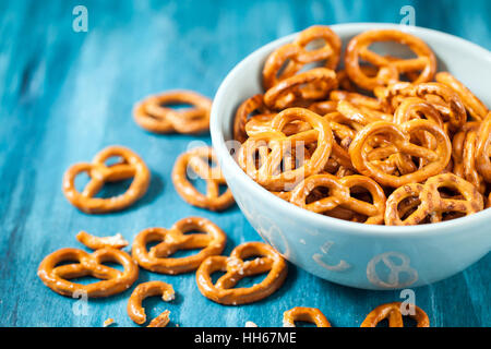 Salty snacks mini pretzels in bowl on blue wooden table Stock Photo