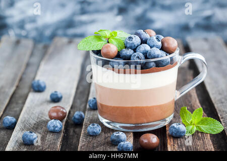 Delicious  three layered chocolate mousse dessert, devorated with fresh blueberry, mint and candies, served in glass cup Stock Photo