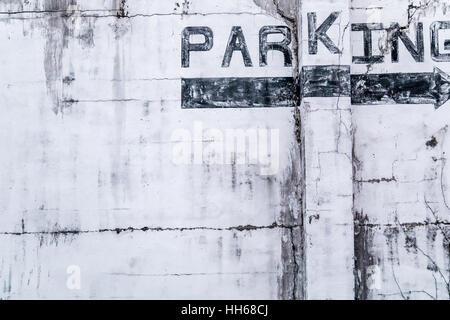 detail of the side of an old building where the word Parking has been painted in black with a black arrow pointing right Stock Photo