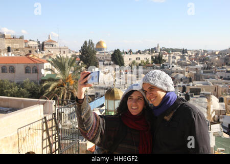 Young man & woman smile as they take selfie above Damascus Gate,  Jerusalem Old City, Mt. of Olives & the Dome of the Rock are in their background. Stock Photo