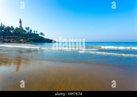 Light house standing above the rocky outcrop above the ocean waves at Kovalam Beach in Kerala, India. Horizontal Stock Photo