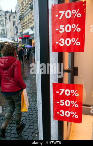red signs on shop window indicate sale and discount percentage and rainy street with people Stock Photo