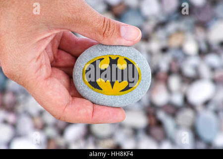 Paphos, Cyprus - November 22, 2016 Sign Batman painted on a pebble in woman hand with stones background. Stock Photo