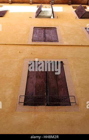 Vintage wooden window shutters. Yellow facade house with wooden shutters. Stock Photo