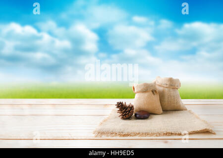 Two of blank hemp sack bag and pine cones on wood table top floor over blur green field and blue sky background with copy space Stock Photo