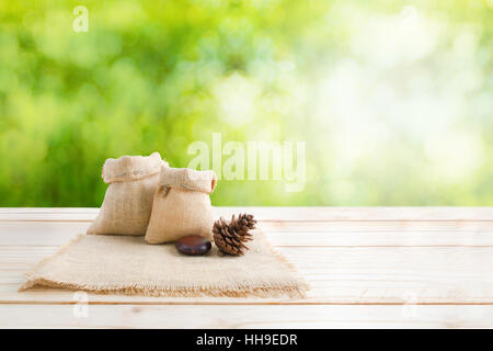 Two of blank hemp sack bag and pine cones on wood table top floor over blur green bokeh background with copy space Stock Photo