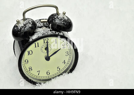 close up of a black retro alarm clock, showing winter time, 2 am, on snow background Stock Photo