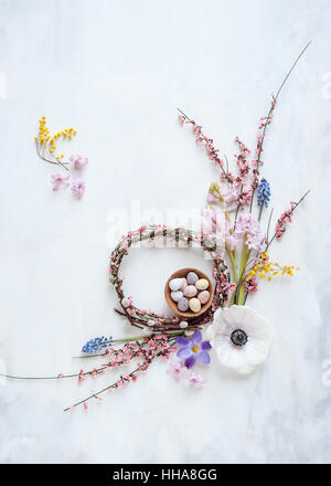 spring wreath with flowers and mini eggs in a bowl, natural light, view from above, laid out on painted white and gray backdrop Stock Photo