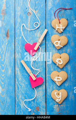 Homemade heart shape cookies and  two red paper hearts  hanging with clothes pegs on string over blue background. Valentines day theme Stock Photo
