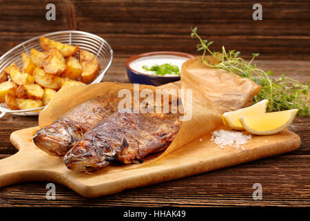 Baked fish with potatoes and white dip on wooden background Stock Photo