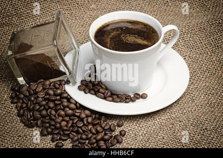 Higher angle view of the vintage photo of the white cup of coffee standing on the sackcloth. Stock Photo