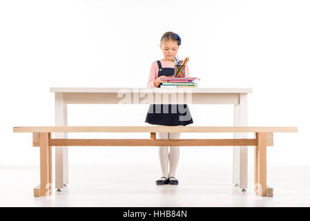 Serious schoolgirl standing at desk and looking on books on white Stock Photo
