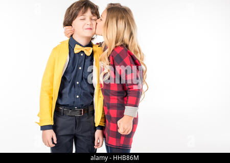 Portrait of schoolgirl hugging and kissing in cheek smiling schoolboy on white Stock Photo
