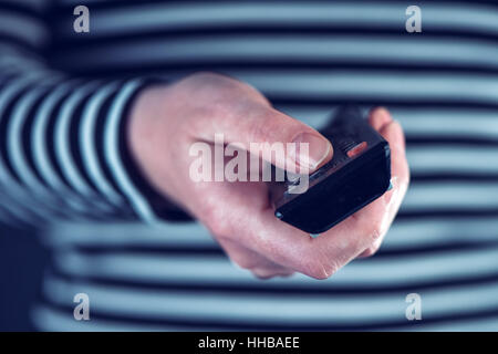Female hand with television remote control pointing to tv set and turning it on or off Stock Photo