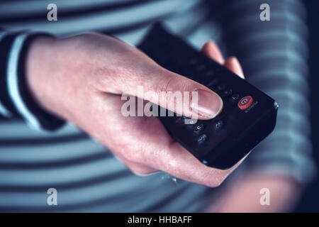 Female hand with television remote control pointing to tv set and turning it on or off Stock Photo
