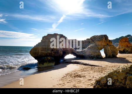 Big rock formation on Olhos De Agua beach, the sun is behind and shining through the natural holes in the rock, this rock formation sits in the middle Stock Photo