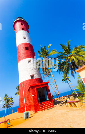 Closeup of red and white striped lighthouse surrounded by palm trees at Kovalem Beach in Kerala Stock Photo
