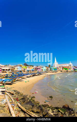 Our Lady of Ransom Shrine Church behind colorful houses on a sand beach occupied by fishing boats in Tamil Nadu. Vertical Stock Photo