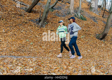 side photo of two sports women jogging in autumn park. Blonde and african girls. Yellow leaves. Female smiling Stock Photo