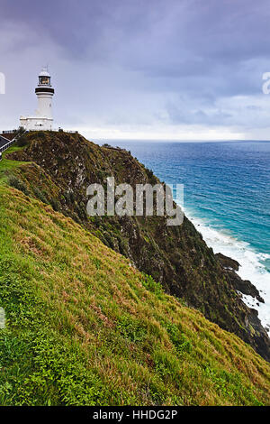 Famous australian Byron Bay lighthouse at the edge of tall cliff of continent mainland against open sea on a cloudy day. Stock Photo