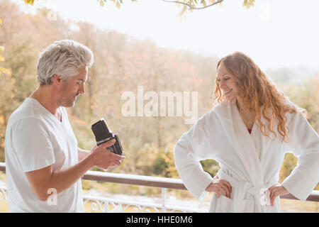 Man with old-fashioned camera photographing woman in bathrobe on autumn balcony Stock Photo