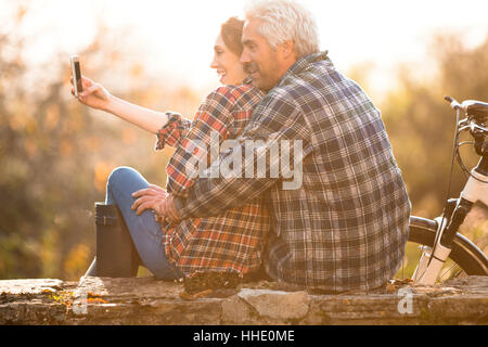 Affectionate couple hugging taking selfie with camera phone in autumn park Stock Photo