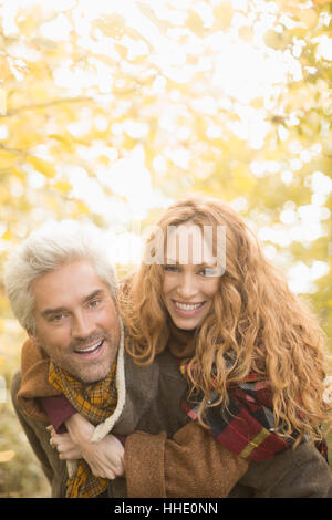 Portrait smiling playful couple piggybacking under autumn trees Stock Photo