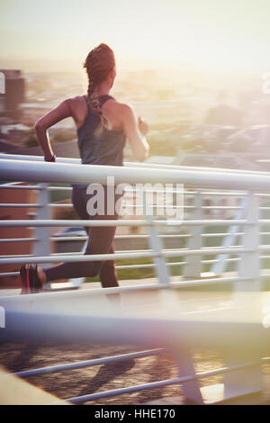 Female runner running on sunny urban footbridge at sunrise Stock Photo