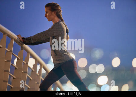 Determined female runner stretching legs on footbridge at dawn Stock Photo