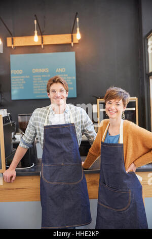 Portrait smiling cafe owners wearing denim aprons in cafe Stock Photo