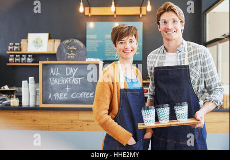 Portrait confident cafe owners in denim aprons holding tray with coffee cups Stock Photo