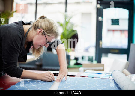 A woman measuring and marking the fabric for an upholstery task in a workshop. Stock Photo