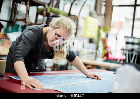 A woman measuring and marking the fabric for an upholstery task in a workshop. Stock Photo