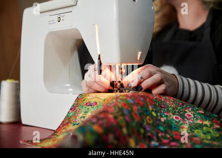 A woman threading a needle on a sewing machine, sewing upholstery fabric. Stock Photo