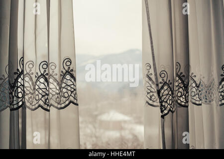 Details of a decorative curtain behind the window, winter mountain landscape in blurry background. Stock Photo