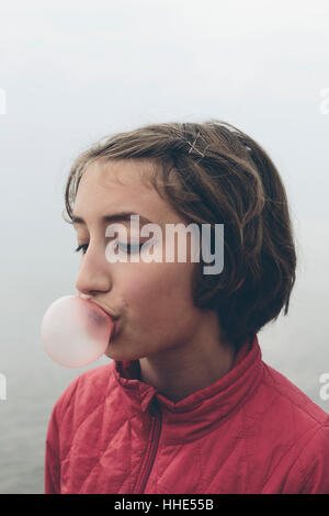 Eleven year old girl blowing bubble gum bubble creating a large pink bubble, childhood skill bubblegum Stock Photo