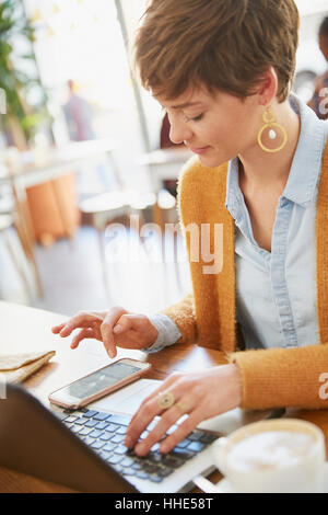 Businesswoman working in cafe using smart phone and laptop Stock Photo