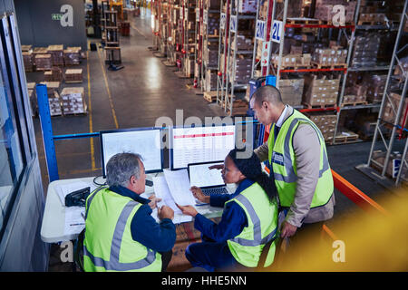 Managers at laptop and computers discussing paperwork in distribution warehouse Stock Photo