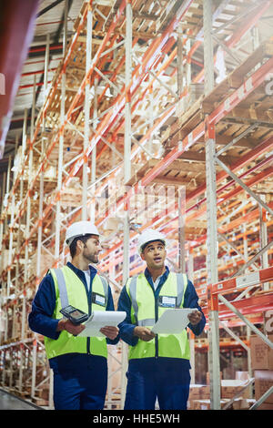 Workers with clipboards and scanner talking in aisle of distribution warehouse Stock Photo
