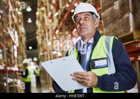 Manager with clipboard checking inventory looking up in distribution warehouse Stock Photo