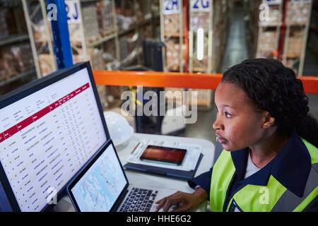 Focused female manager using laptop and computer in distribution warehouse Stock Photo