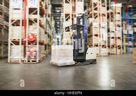 Worker operating forklift moving pallet of boxes in distribution warehouse Stock Photo