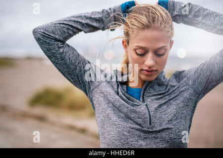 Fit female athlete tying hair before her workout outdoors. Young woman getting ready for training. Stock Photo
