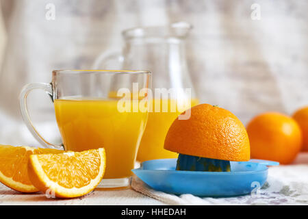 Plastic juicer with glass of fresh orange juice on white rustic wooden background. Copy space Stock Photo