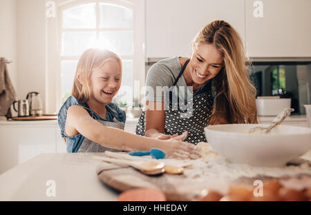 Happy young girl with her mother making dough. Mother and daughter baking in kitchen. Stock Photo