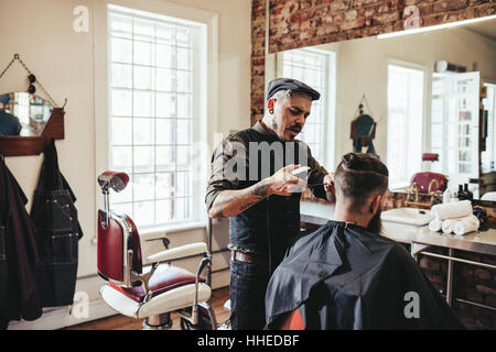 Hairstylist serving client in salon. Young man getting trendy haircut at barbershop. Stock Photo