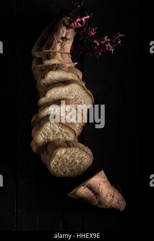 Sliced Brown Sweet Potato with Purple Sprouts on Black Wood Stock Photo
