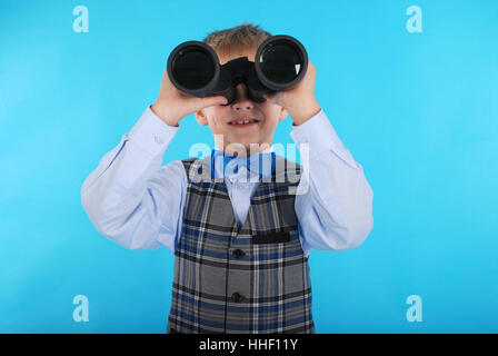 Curious schoolboy looking through binoculars. Photos on a blue background Stock Photo